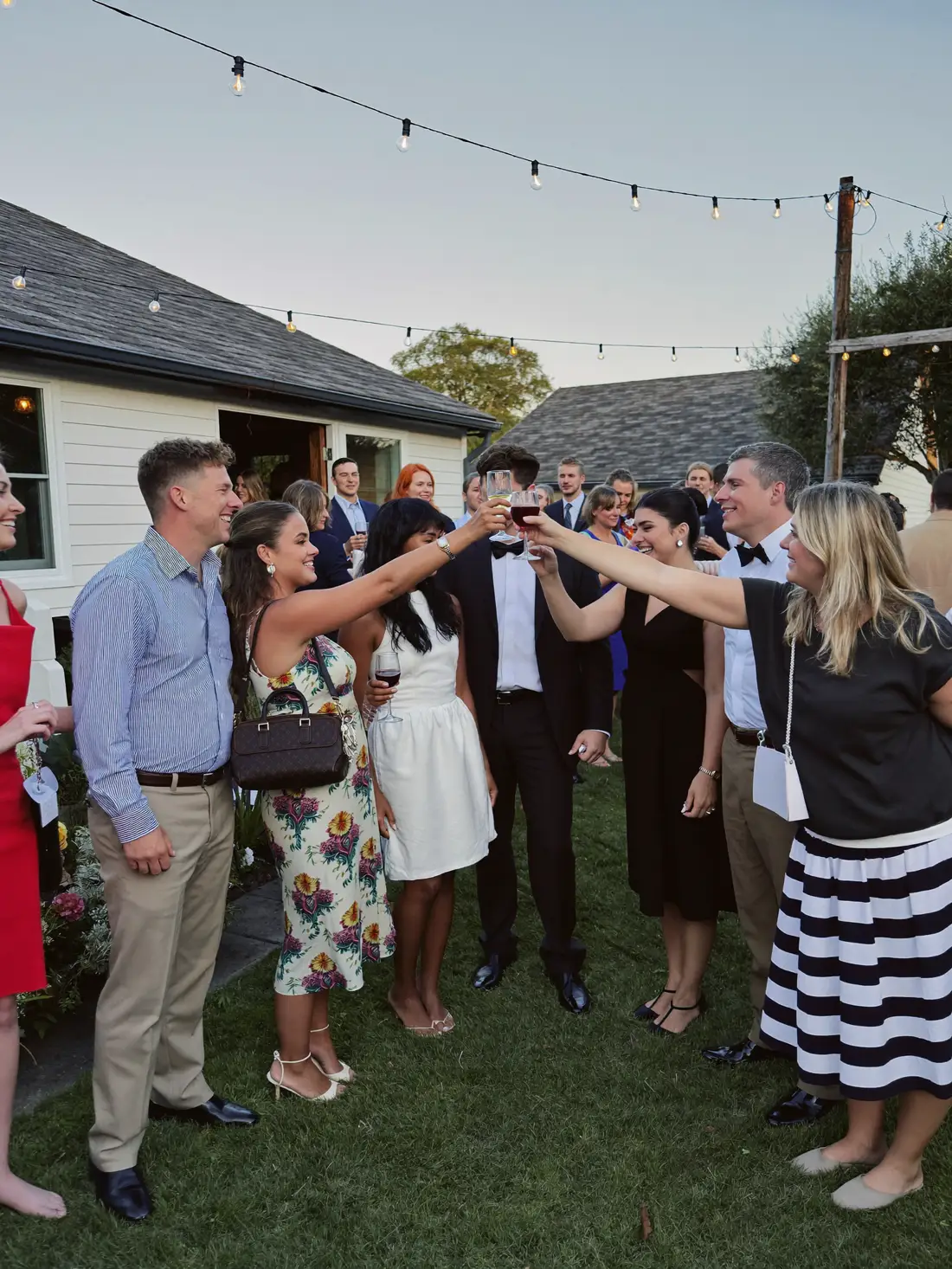 Friends toasting at a backyard wedding under string lights